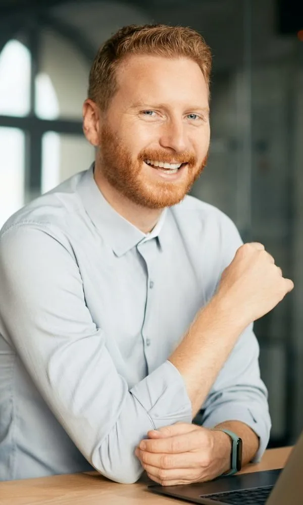 happy-entrepreneur-using-laptop-while-working-at-corporate-office-and-looking-at-camera--e1682661111904